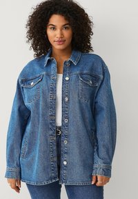 Giubbotto in denim di lavaggio medio, con chiusura a bottoni, due tasche sul petto e una vestibilità comoda. Il tessuto testurizzato ne esalta l'aspetto complessivo.