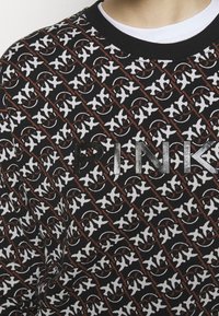 Czarna bluza z powtarzającym się białym wzorem i brązowymi akcentami. Na przodzie widnieje napis "PINK" w metalicznym piśmie.