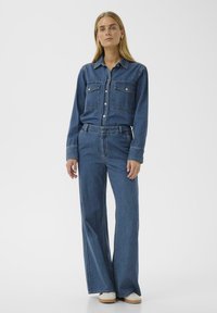 Denim shirt with button closure, two chest pockets, and long sleeves paired with high-waisted wide-leg jeans in medium blue. White sneakers.