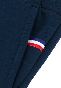 Tessuto blu navy con una superficie liscia; presenta un bordo con strisce rosse, bianche e blu vicino alla cucitura come accento.