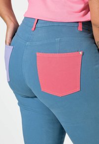 Modré džíny s hladkou texturou, s růžovým a levandulovým zadním kapsou. Obsahují kontrastní švy a detail poutka na opasek.