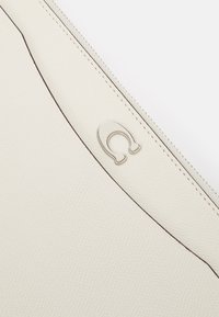 Vit läderpouch med en texturerad yta, mörka sömmar och en silverfärgad metallaccent vid dragkedjan.