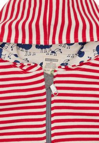 Felpa con zip a righe rosse e bianche, con zip grigia e foderatura con motivo a formiche blu. Realizzata in cotone 100% biologico.