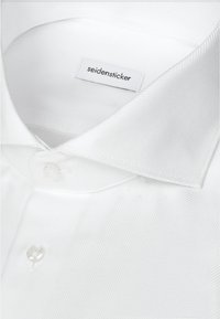 Chemise blanche avec texture en chevrons, col à boutons et étiquette de marque "seidensticker" à l'intérieur du col.