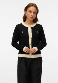 Cardigan nero con accenti crema, caratterizzato da bottoni dorati e polsini a coste. Due tasche sul petto con linee orizzontali. Texture a maglia morbida.