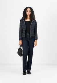 Zwarte gewatteerde pufferjas met capuchon, gecombineerd met donkerblauwe rechte spijkerbroek en zwarte schoenen, met een kleine zwarte handtas.