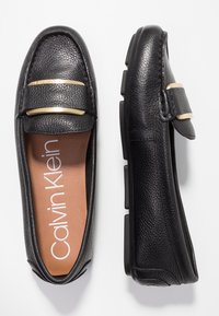 Mocassins en cuir noir à finition texturée, dotés d'une bride accentuée en or, d'une semelle intérieure rembourrée et d'une semelle extérieure en caoutchouc conçue pour le confort.