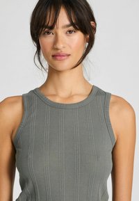 Top a maniche corte di colore verde scuro, con un collo rotondo e senza maniche. Il tessuto ha una superficie liscia e linee verticali sottili.