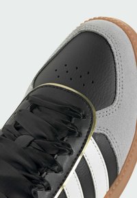 Čierne a šedé tenisky s textúrovaným koženým zvrškom, bielymi pruhmi a zlatými detailmi. Majú zaoblenú špičku a ploché šnúrky.