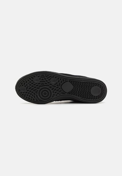 Black rubber sneaker sole with textured grip pattern, including circular and ridged elements for traction. Rounded edge and contoured design.