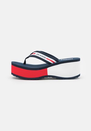 Laivastonsininen, valkoinen ja punainen platfom-sandaali, jossa paksu pohja ja kangasremmi, jossa on teksti "JEANS" ja raidat.