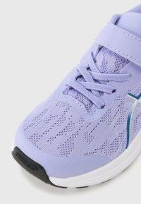 Μωβ αθλητικό παπούτσι με ανώτερο μέρος από δίχτυ, έντονες μπλε λεπτομέρειες και επενδεδυμένο περιλαίμιο. Διαθέτει κορδόνια και ιμάντα με αγκράφα για ασφαλή εφαρμογή.