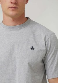 Camiseta de algodón gris con cuello redondo y mangas cortas. Presenta un pequeño logo en navy en el pecho, con un tejido texturizado y suave.