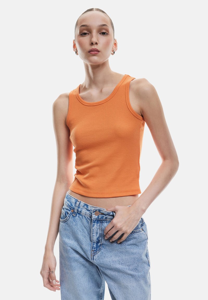 Oranje geribde tanktop met een ronde halslijn en een getailleerd ontwerp. Gecombineerd met hoge taille, lichtblauwe spijkerbroek.