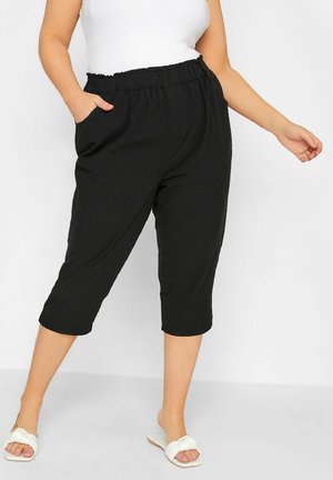 Woman wearing black cropped pants with elastic waist and side pockets, paired with white top and white slide sandals.