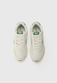 White mesh sneakers with green accents, featuring a padded collar, structured lacing, and textured rubber sole. Brand logo on tongue.