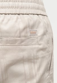 Μπεζ σορτς από υφή υφάσματος με ελαστική μέση, πίσω τσέπη και μικρή ετικέτα "BOSS" πάνω από την τσέπη.