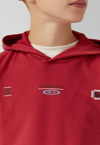 Rode sweatshirt met capuchon. Bevat tekstversieringen in het wit en blauw, waaronder "GOOD ENERGY" en "SOUNDTRACK OF MY LIFE VOL. 8."