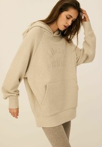 Beżowa, oversize bluza z kapturem, z kieszenią kangurzą, z wytłoczonym tekstem "Diners Athletes" z przodu oraz prążkowanymi mankietami dla uzyskania tekstury.