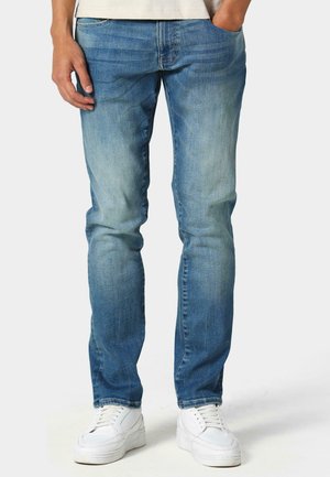 Vaqueros de denim azul claro con un corte recto, que presentan detalles en los bolsillos y un ligero desvanecido. Combinados con zapatillas blancas, el conjunto es casual.