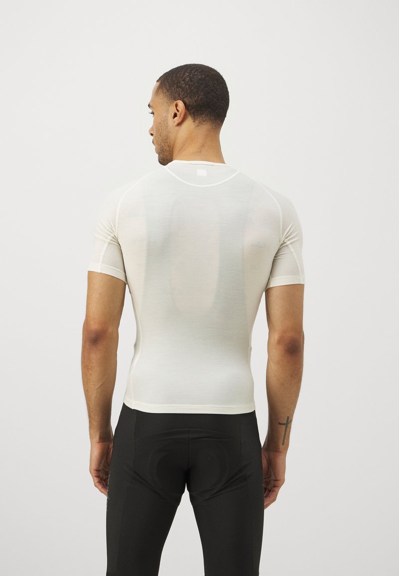 T-shirt de sport blanc, ajusté, à manches courtes, avec des coutures minimales et un col arrondi. Porté avec un pantalon de sport noir, mettant en valeur une texture lisse.