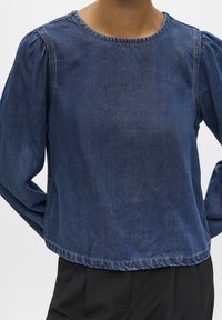 Denim majica s okruglim izrezom, obrađenim rukavima i blago skraćenim krojem. Tamnoplava boja s vidljivim šavovima.