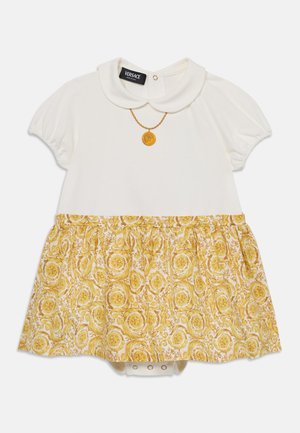 Vestido branco de manga curta com uma saia de padrão floral amarelo, apresentando um colarinho e um detalhe de medalhão dourado na gola.