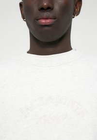 Bílá mikina s kulatým výstřihem zdobená tónovým výšivkou "JACK & JONES 1990". Měkká textura a volný střih, vhodná pro každodenní nošení.