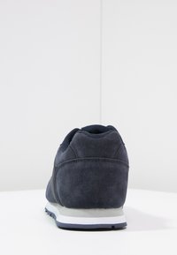 Marinblå mockasneakers med en slät struktur, vit mellansula och vadderad krage. Har en sydd design och minimal märkning på baksidan.