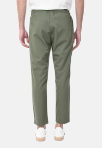 Pantaloni verde oliva con vita elastica, gamba affusolata e texture liscia, abbinati a sneakers bianche e un design sobrio.