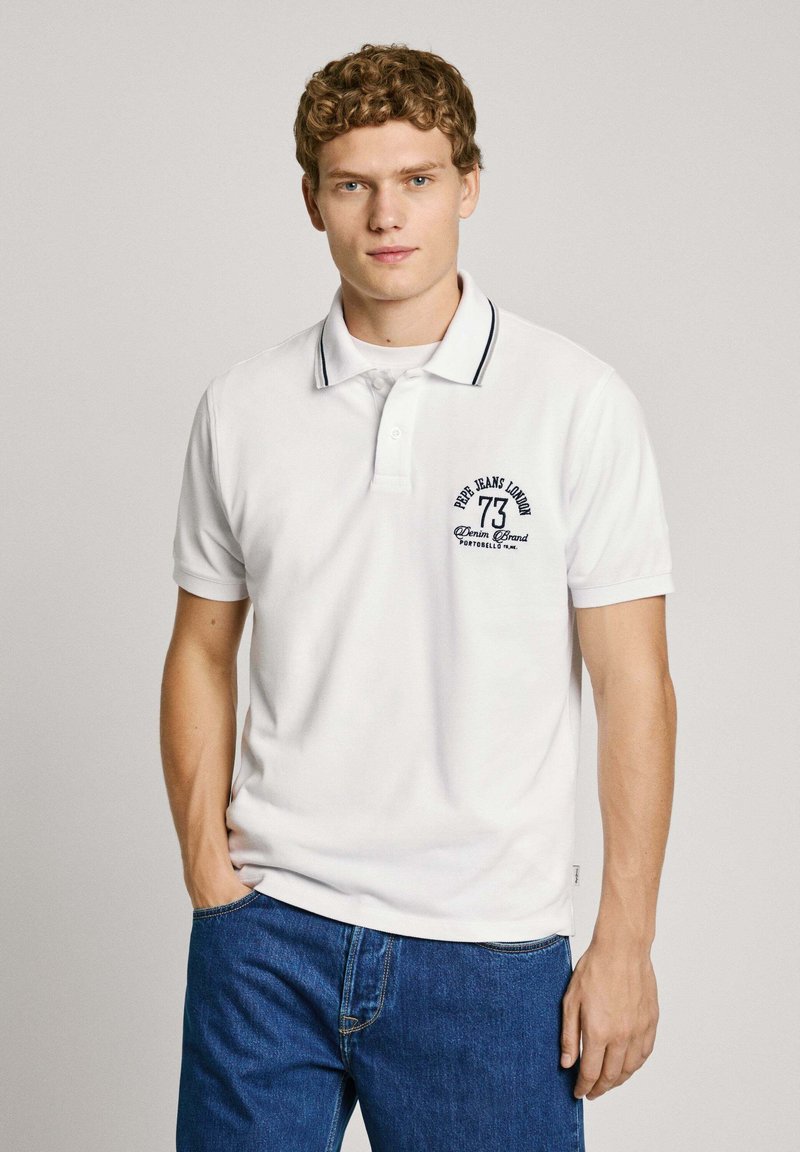 Balts polo krekls ar kontrastējošu tumši zilu apkakli, ar izšūtu logotipu un numuru uz kreisā krūšu. Gluda tekstūra, īsas piedurknes.