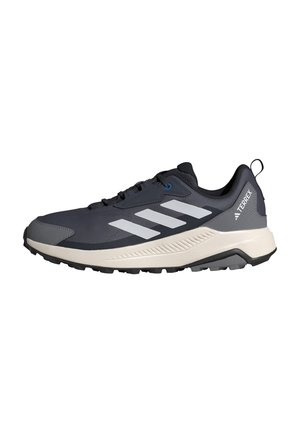 Dunkelgrauer und schwarzer Adidas Terrex Trailrunning-Schuh mit weißen Streifen und robuster Sohle, Seitenansicht vor weißem Hintergrund.
