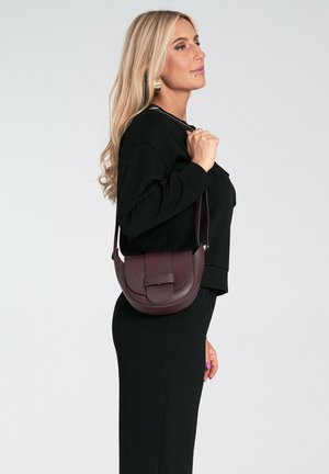 Bordowa skórzana torebka na ramię o zaokrąglonym kształcie, plecionej fakturze i płaskim zapięciu. Regulowany pasek i minimalistyczne elementy metalowe.