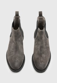 Botas Chelsea de ante gris con paneles elásticos en los lados, punta redonda y suela de goma negra. Cuenta con una pestaña en el talón para una fácil puesta.