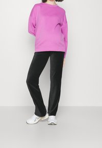 Růžová oversized mikina s spadlými rameny, spárovaná s černými manšestrovými kalhotami a bílými sportovními botami. Jednoduchý, casual design outfitu.