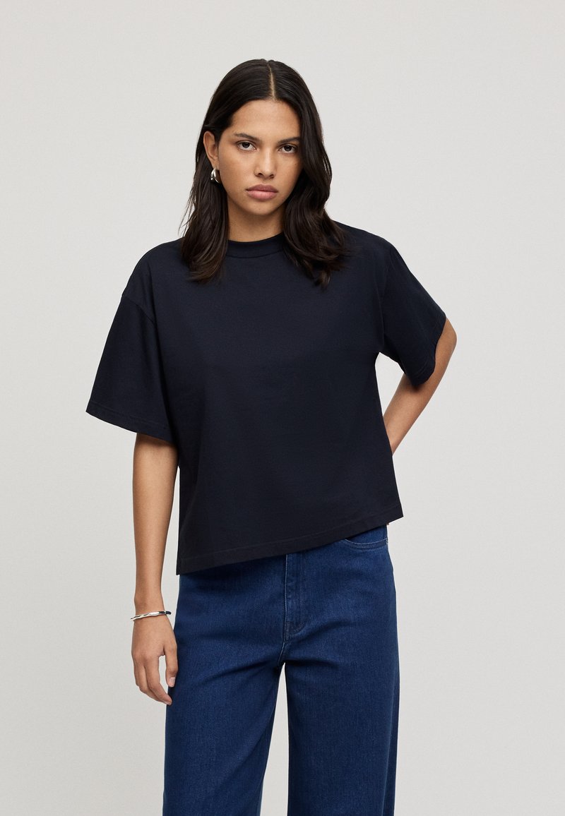Black short-sleeved t-shirt with a round neckline, featuring a relaxed fit and soft cotton material. Combined with blue wide-leg jeans.