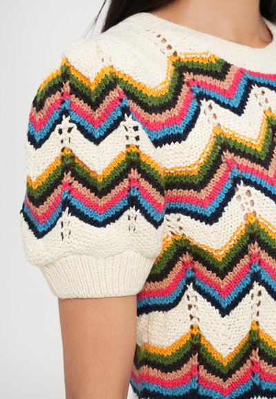 Pull en tricot avec une base crème et des motifs en zigzag multicolores dans les tons rose, bleu, vert et marron. Manches courtes bouffantes avec des poignets côtelés.