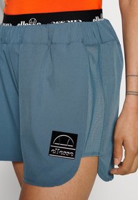 Blå shorts i lätt material med rullad midja, med en svart logopatch och sidofickor för rörelsefrihet.