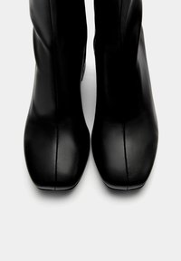 Bottes noires à la cheville en cuir lisse avec un bout carré. Présentent un design minimaliste et une fermeture éclair latérale pour un enfilage facile.
