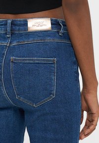 Τζιν παντελόνι ψηλόμεσο σε σκούρο μπλε χρώμα, με δερμάτινη ετικέτα στη μέση και πίσω τσέπη με διπλό ράψιμο. Ομαλή υφή.