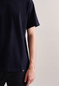 T-shirt in cotone blu navy con maniche corte, collo a giro, vestibilità comoda, design semplice, caratterizzato da un piccolo etichetta con logo sull'orlo.