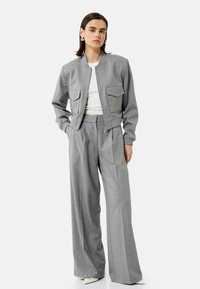 Szara, dopasowana bomberka z dwoma przednimi kieszeniami, w połączeniu z szerokimi szarymi spodniami. Obie części mają gładki, teksturowany materiał.