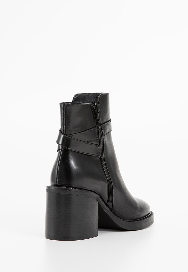 Stivaletto in pelle nera con tacco a blocco spesso, zip laterale e dettaglio decorativo a fascia intorno alla caviglia.