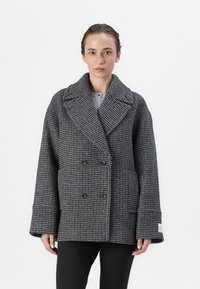Dobbeltbrystet uldfrakke i sort og grå houndstooth-mønster, med brede revers, store knapper og oversized ærmer.