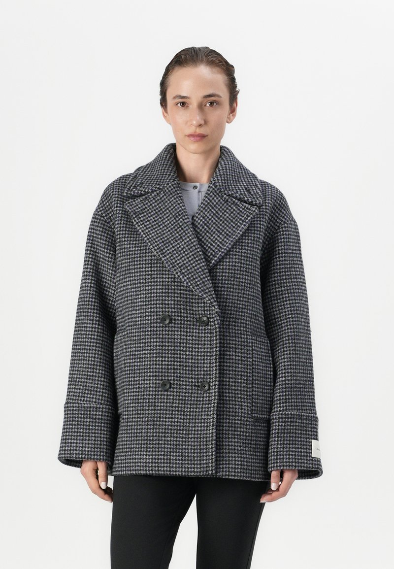 Dobbeltbrystet uldfrakke i sort og grå houndstooth-mønster, med brede revers, store knapper og oversized ærmer.