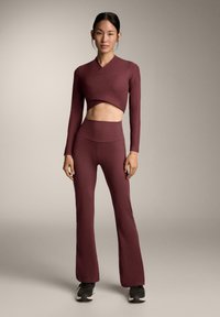 Bordeauxroze fitnessset met een cropped top met lange mouwen en high-waisted wijde broek. Gestructureerde stof, aangesloten silhouet en minimale naden.