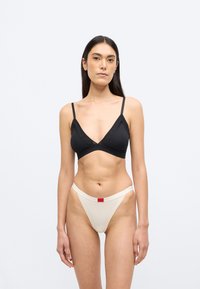 Czarny biustonosz typu bralette z cienkimi ramiączkami i głębokim dekoltem w kształcie litery V, w połączeniu z kremowym stringami z czerwoną metką z logo na pasku.