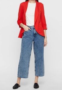 Punainen bleiseri valkoisen t-paidan päällä, yhdistetty korkeavyötäröisiin, leveälahkeisiin sinisiin farkkuihin. Mustat slip-on-kengät viimeistelevät asun.