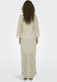 Kimono de ganchillo largo, color crema, con mangas amplias y patrón calado, que se alarga hacia la parte posterior. Material texturizado y ligero.