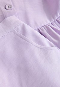 Levendulalila, gombos női ruha, puha anyagból, összehúzott derékrésszel és oldalzsebbel. Sima anyag, könnyű kialakítás.